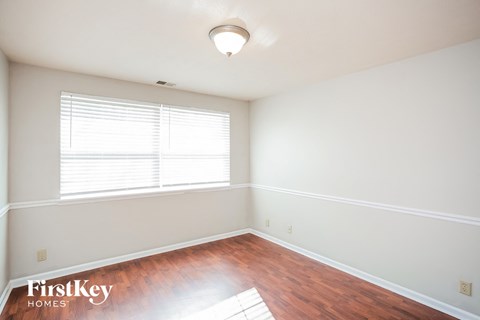a bedroom with white walls and wood floors and a window
