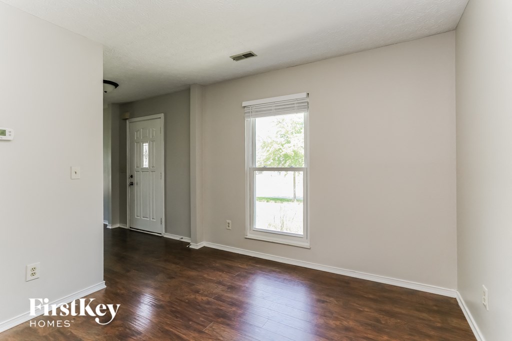 a living room with wood floors and white walls and a window