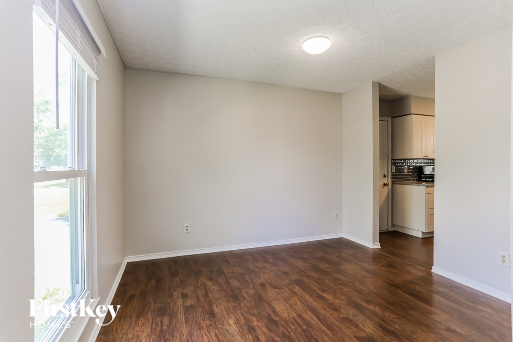 an empty living room with wood flooring and a kitchen