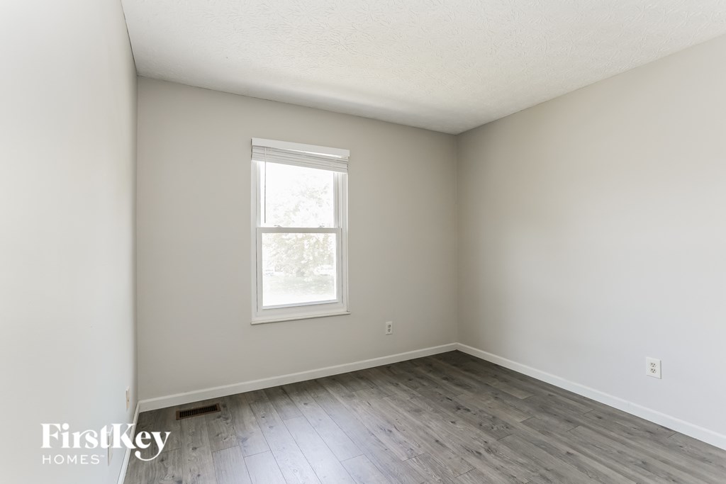 a bedroom with white walls and wood floors and a window
