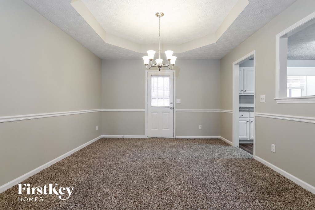 an empty dining room with carpet and a door to the kitchen