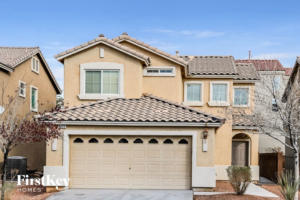 A beige house with a brown roof and a white garage door.