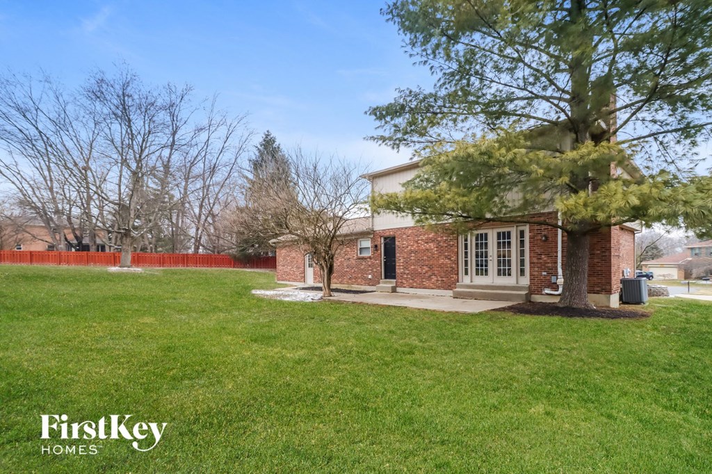 the front of a brick house with a lawn and a tree