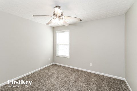 the spacious bedroom with carpeted flooring and a ceiling fan