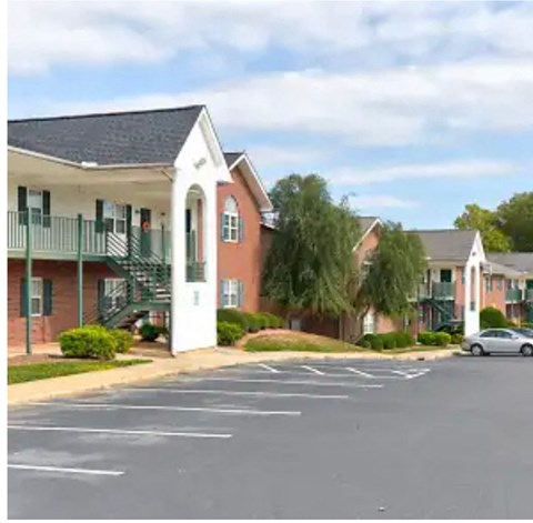 A car is parked in a parking lot in front of a red brick building with a white door and green trim.
