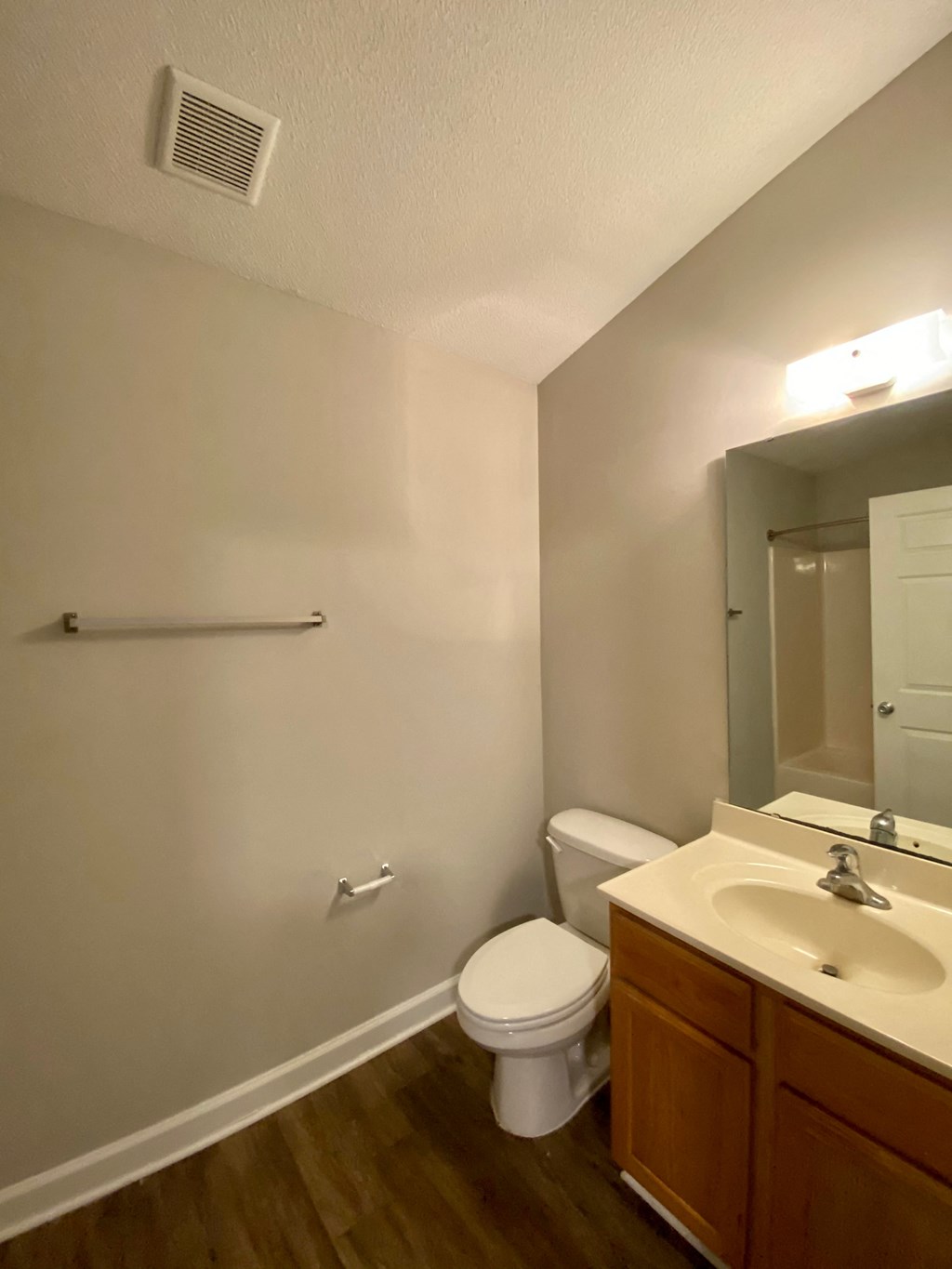 A bathroom with a toilet, sink, mirror, and a towel bar.