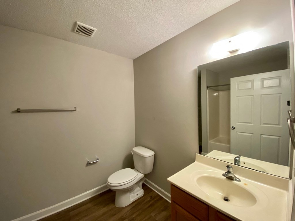 A bathroom with a toilet, sink, mirror, and a towel bar.