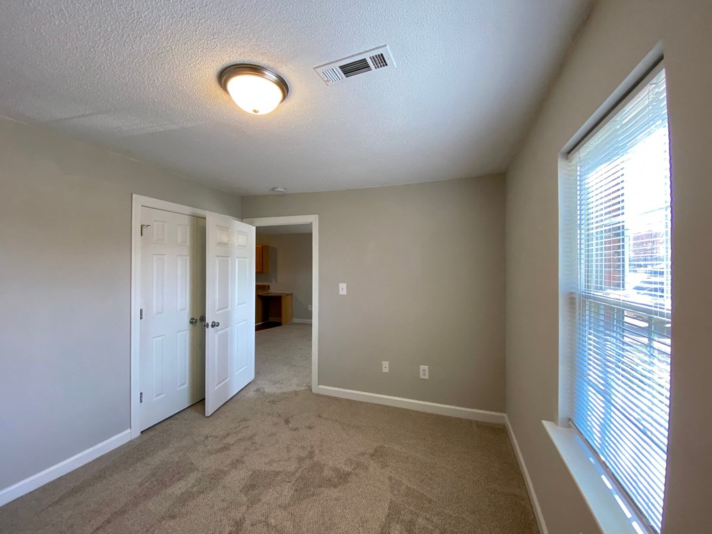 A room with carpeted floor and a window with blinds.
