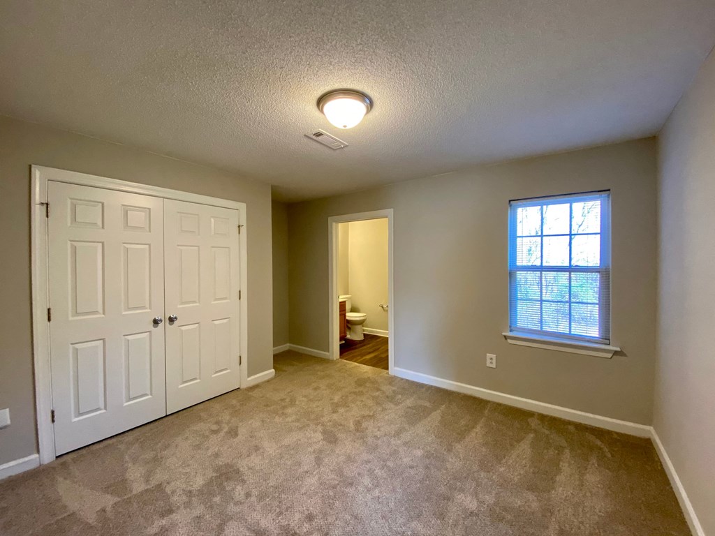 A room with a carpeted floor, a white door, and a window with blinds.