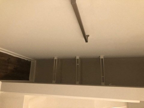 A white shelf with a black pipe running along the ceiling.