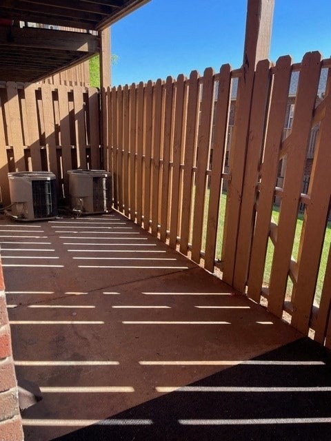 A wooden fence and two air conditioning units are in a parking lot.