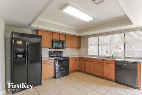 A kitchen with a black fridge, black oven, black dishwasher, and wooden cabinets.