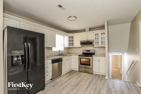 A black refrigerator with the words "FirstKey Homes" on it is in a kitchen with white cabinets.