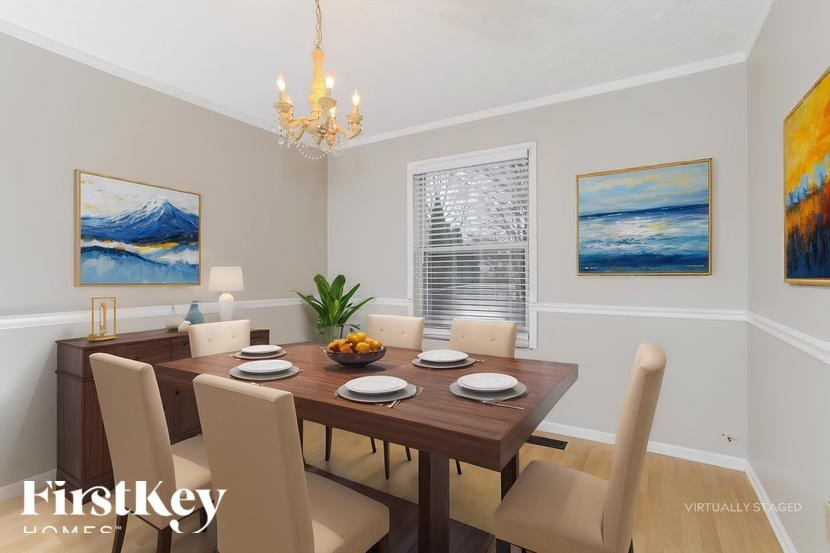 A dining room with a wooden table and chairs, a chandelier, and a painting on the wall.