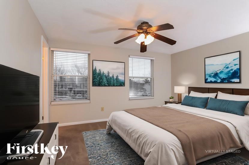 A bedroom with a bed, a ceiling fan, and two pictures on the wall.