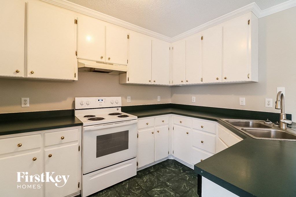 a kitchen with white cabinets and black counter tops and a white stove and sink