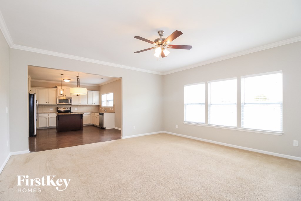 A spacious living room with a ceiling fan and a kitchen in the background.