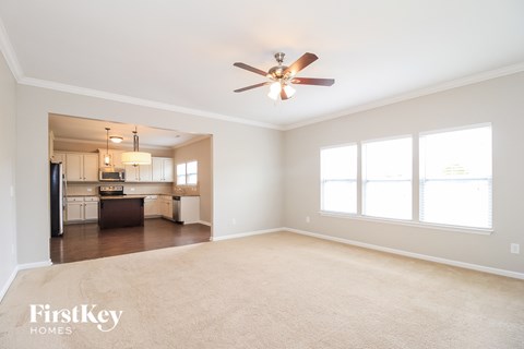 A spacious living room with a ceiling fan and a kitchen in the background.