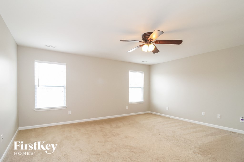 A spacious room with a ceiling fan and two windows.