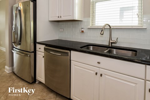 A kitchen with a stainless steel refrigerator and a black countertop.