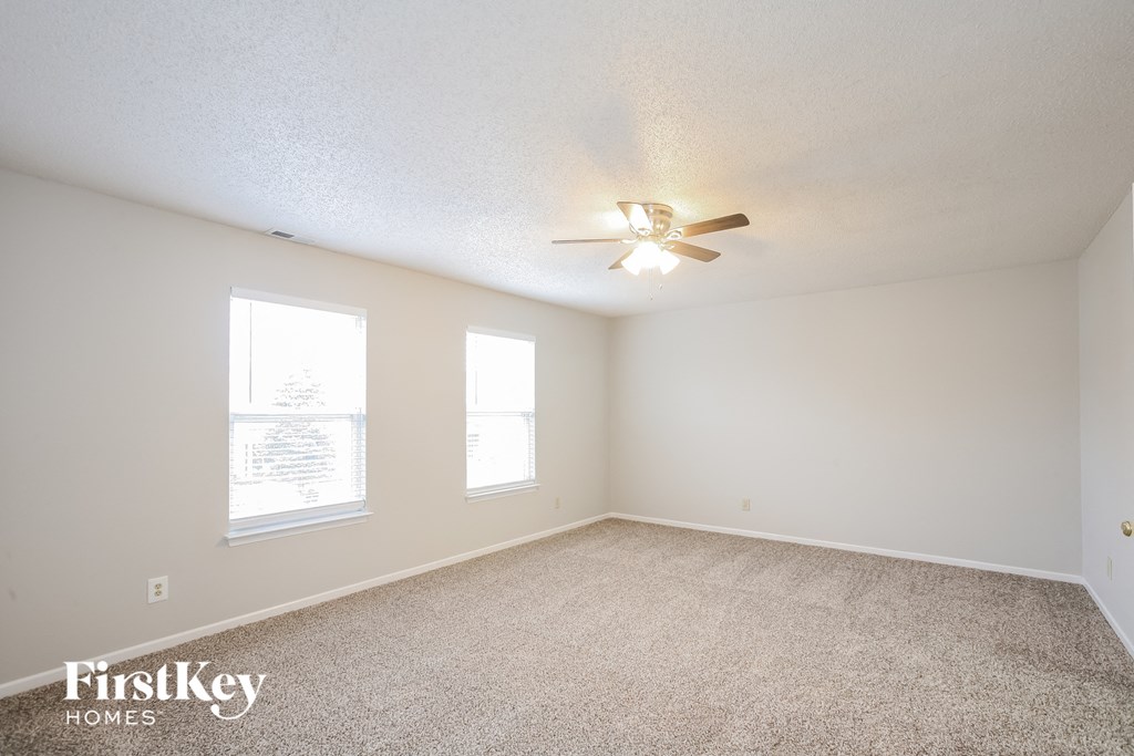 the spacious living room with ceiling fan and carpeting