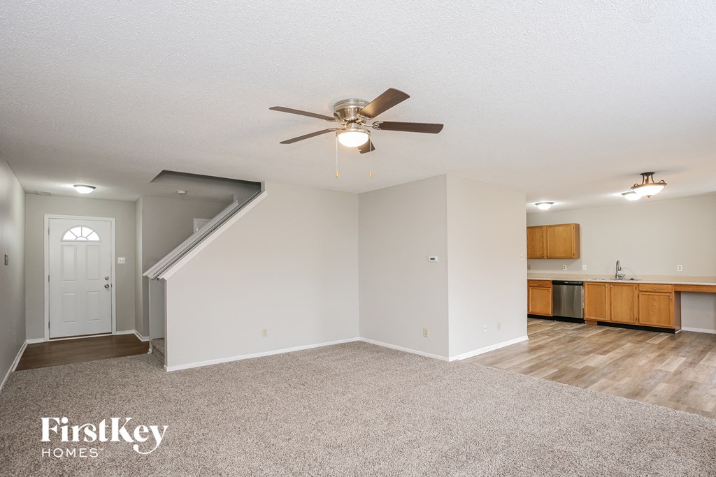 an empty living room with a ceiling fan and a kitchen