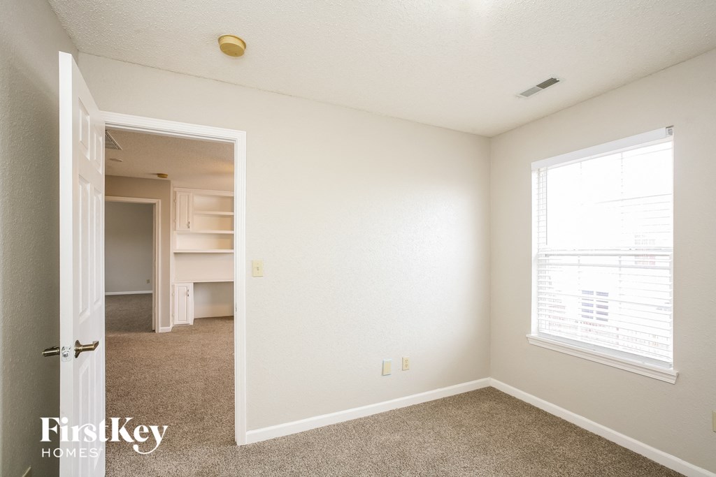 a bedroom with white walls and carpet and a door to a closet