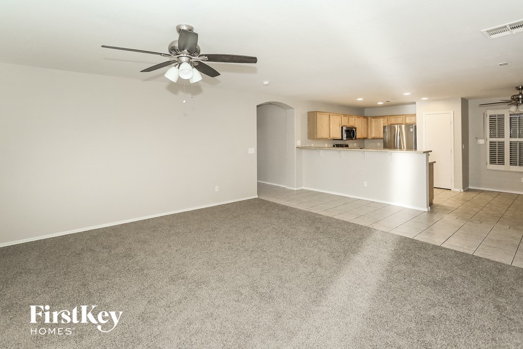 A spacious room with a ceiling fan and a kitchen area in the background.