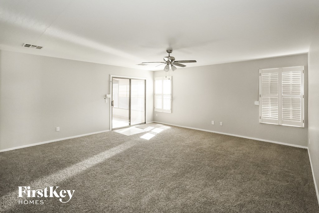 A spacious room with a carpeted floor, a ceiling fan, and a sliding glass door leading to another room.