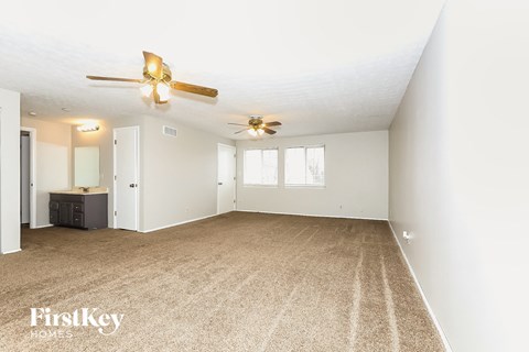 A spacious room with a carpeted floor and a ceiling fan.