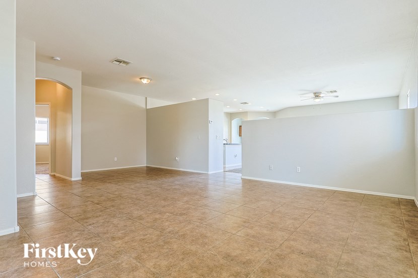 A spacious room with beige tiled flooring and white walls, with a ceiling fan and a doorway leading to another room.