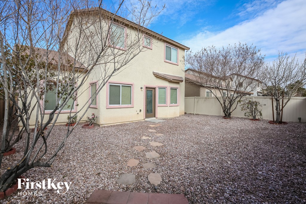 a beige house with green shutters and a gravel driveway