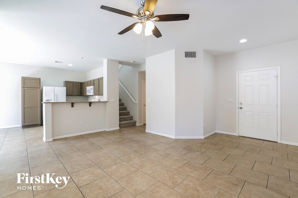 an empty living room with a ceiling fan and a kitchen
