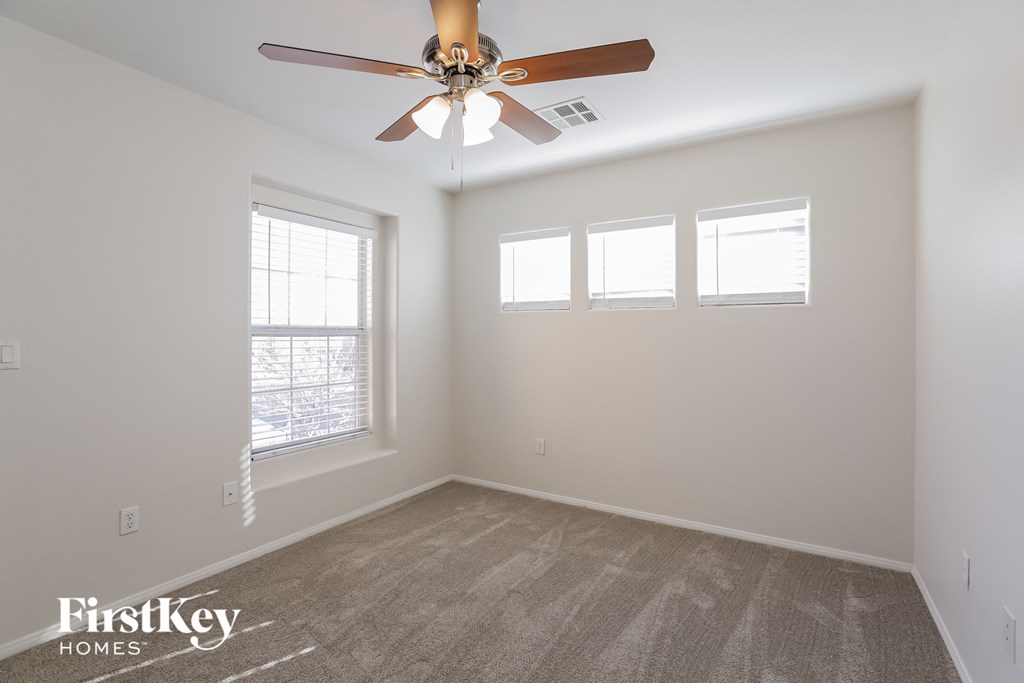 an empty room with a ceiling fan and three windows