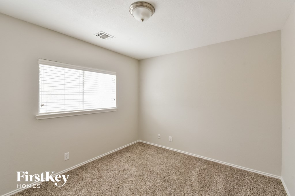the spacious bedroom has carpeted floors and a window