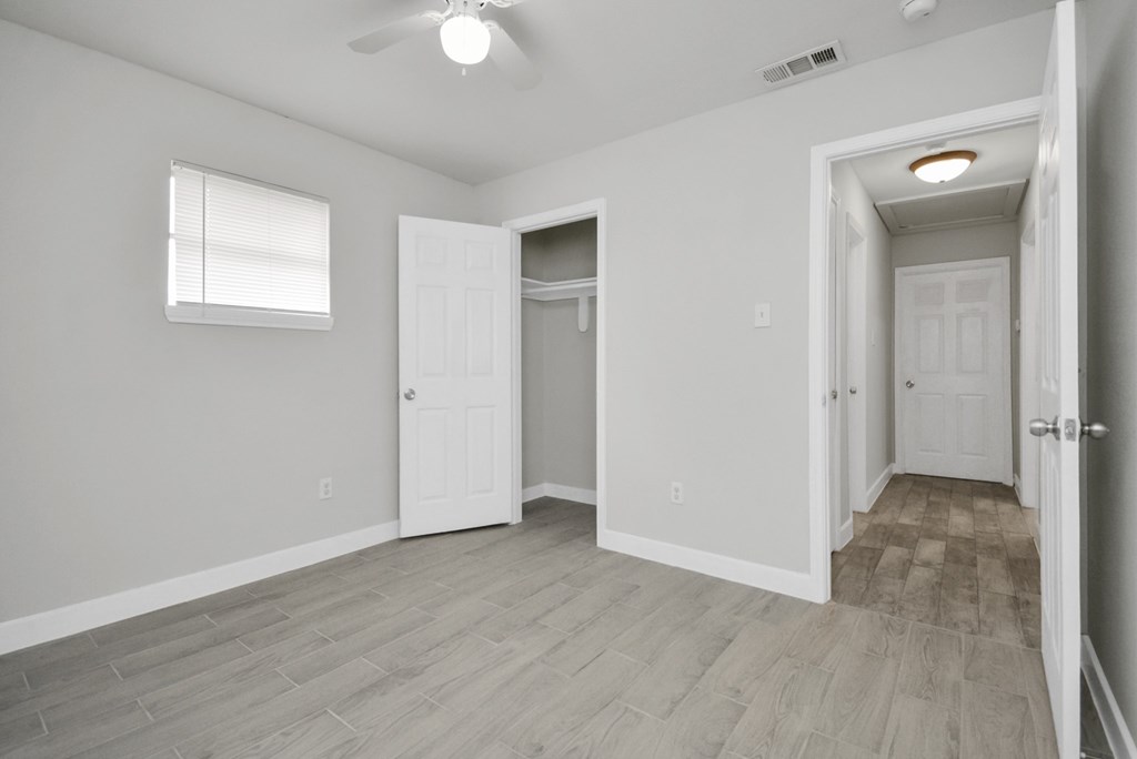 A room with a ceiling fan and light, a window with blinds, and a door leading to another room.