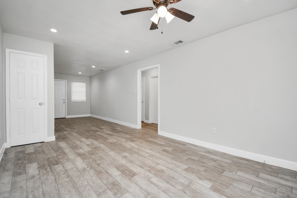 A room with a ceiling fan and lighting fixture, and a wooden floor.