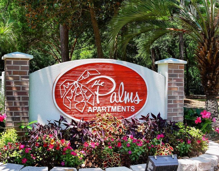 a sign for the palmas apartments in front of a garden