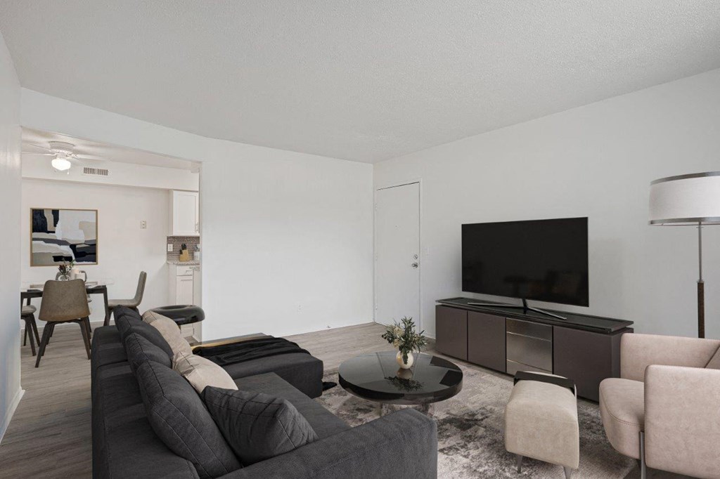 A modern living room with a black sofa, a grey armchair, a black coffee table, a black television, and a white wall.