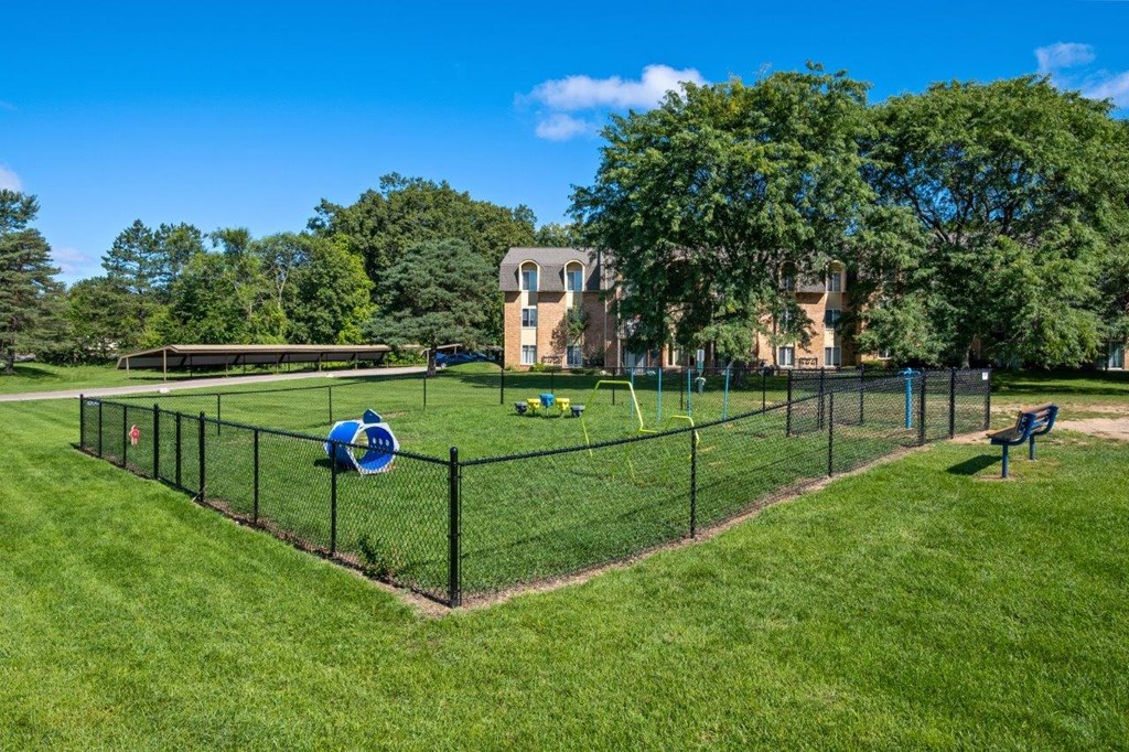 A park with a fence, a blue ball, and a bench.
