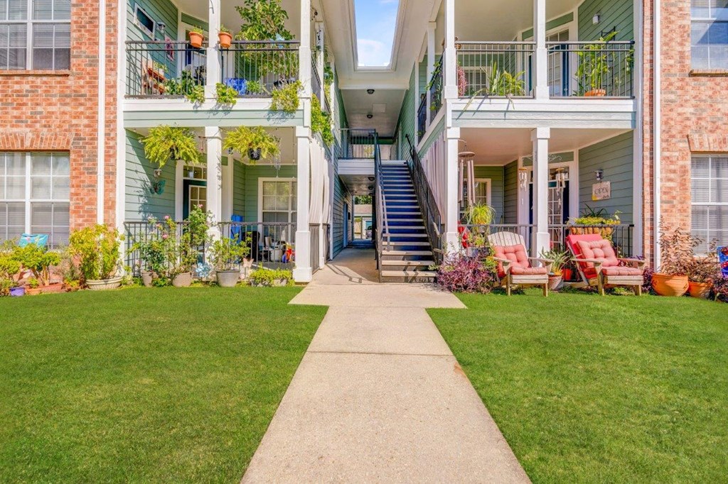 a sidewalk in front of a house with a yard and stairs