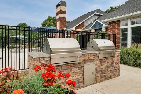 two barbecue grills on a stone wall in front of a house
