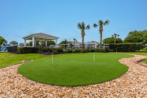 a putting green with palm trees and a house in the background