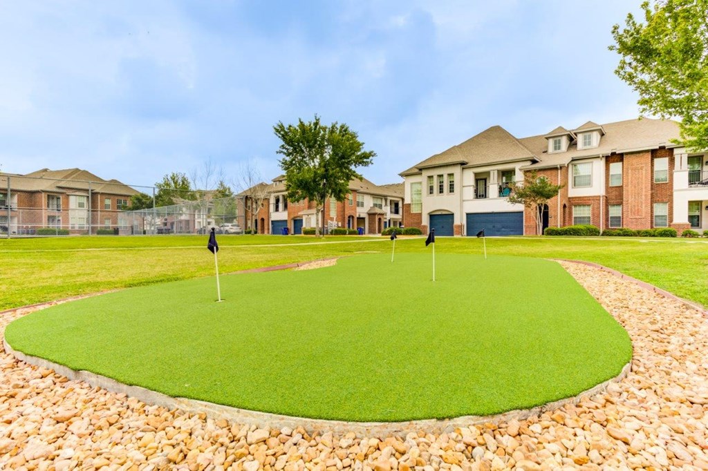 an artificial turf putting green with houses in the background