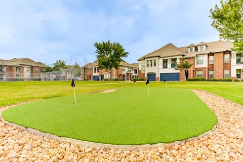 an artificial turf putting green with houses in the background