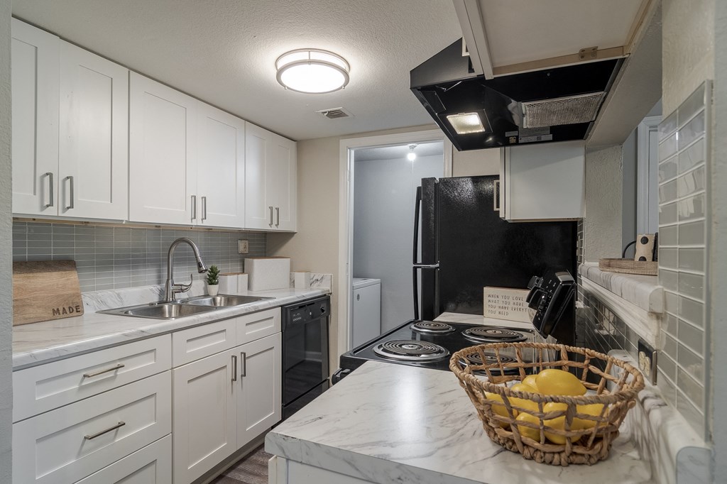 a kitchen with white cabinets and black appliances and a basket of fruit