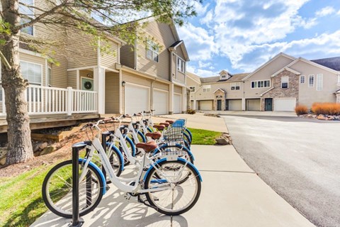 A row of bicycles are parked on a sidewalk in front of apartment buildings.