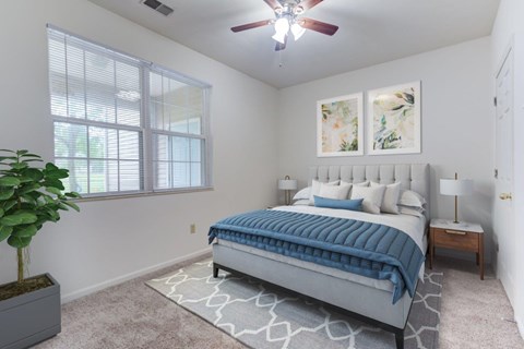 A bedroom with a bed, a ceiling fan, and a potted plant.