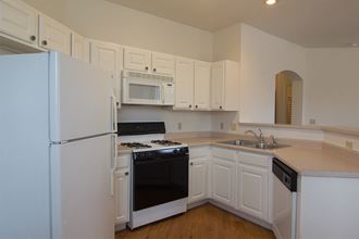 an empty kitchen with white cabinets and appliances and a refrigerator