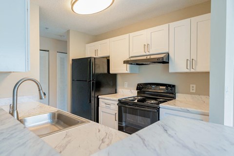 A kitchen with a black refrigerator, stove, and white cabinets.